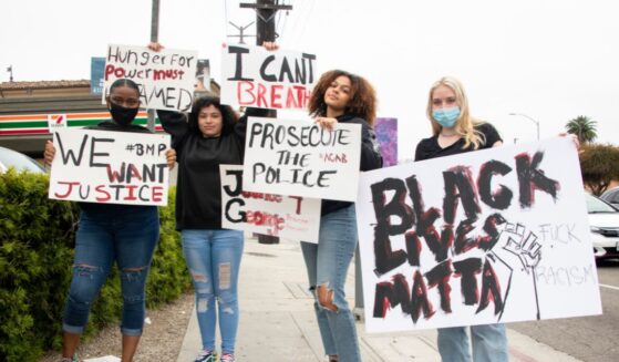 Young women wear protective masks and hold signs in support of Black Lives Matter on May 28, 2020, in Marina del Rey, California.