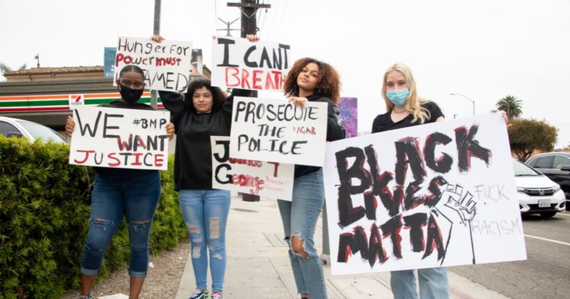 Young women wear protective masks and hold signs in support of Black Lives Matter on May 28, 2020, in Marina del Rey, California.
