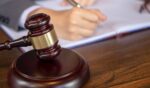 A person writes on a page as a gavel sits next to them.