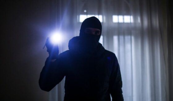 A burglar shines a bright flashlight in a dark house.