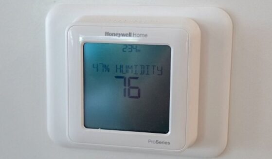 Pictured in a white room a Honeywell thermostat can be seen on a wall at 76 degrees.