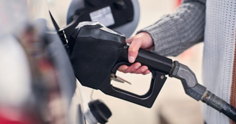 A woman grabs gas pump at a gas station.