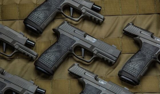 Pistols are laid out on a brown fabric in a pattern.