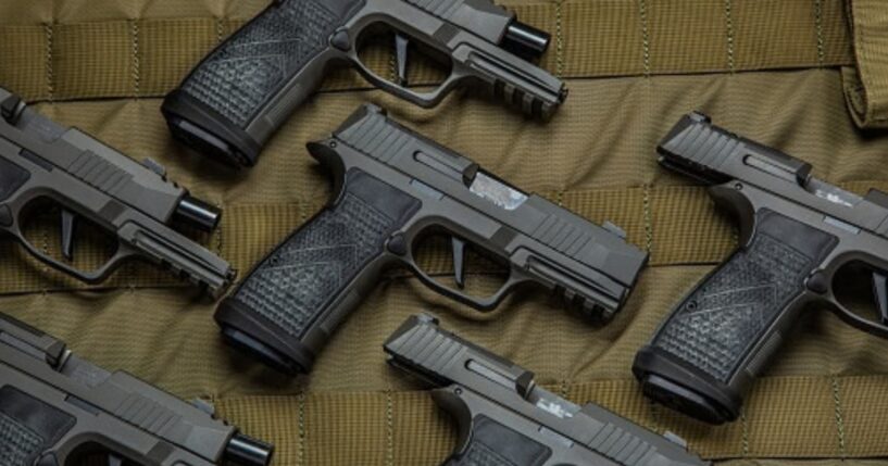 Pistols are laid out on a brown fabric in a pattern.
