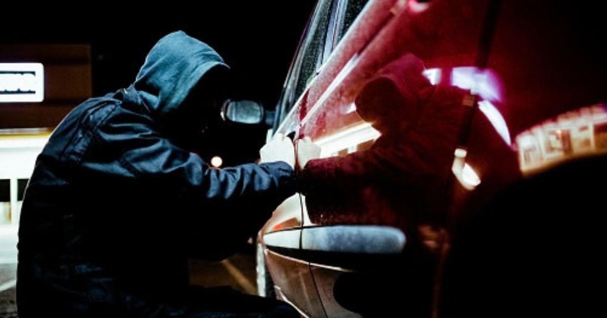 A thief tries to pry open a car door.
