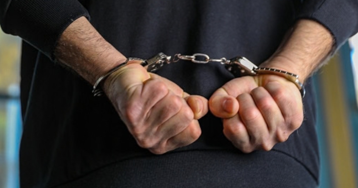 A man is pictured handcuffed in a dark blue shirt.