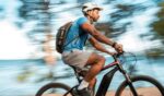 A man rides his electric bicycle on a trail near a body of water.