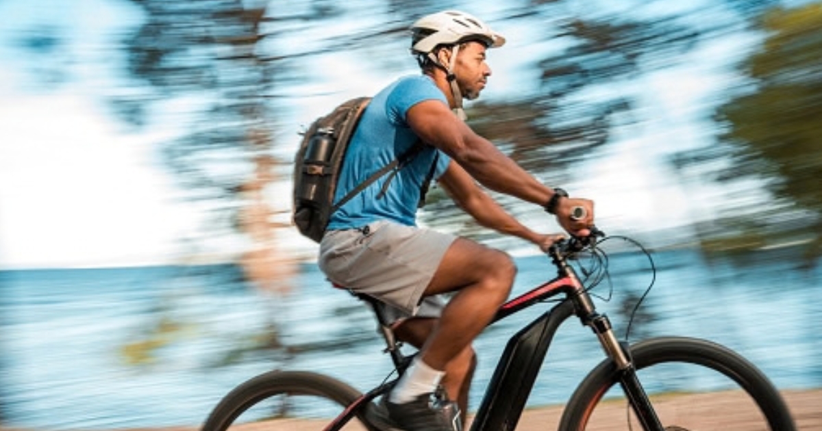 A man rides his electric bicycle on a trail near a body of water.