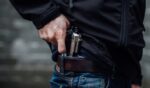 A man pulls a gun from his jeans pocket.