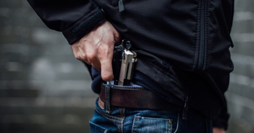 A man pulls a gun from his jeans pocket.
