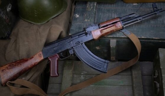 An AK-47 rifle lays on a military box above ammunition.