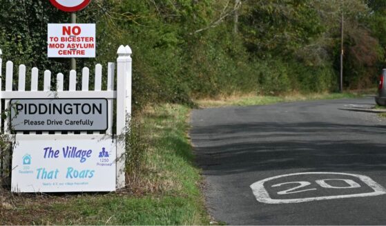 A sign for the village of Piddington, England, is pictured next to another saying 'No to Bicester MOD asylum centre,' in reference to a government plan to house some 1,200 male asylum seekers nearby.