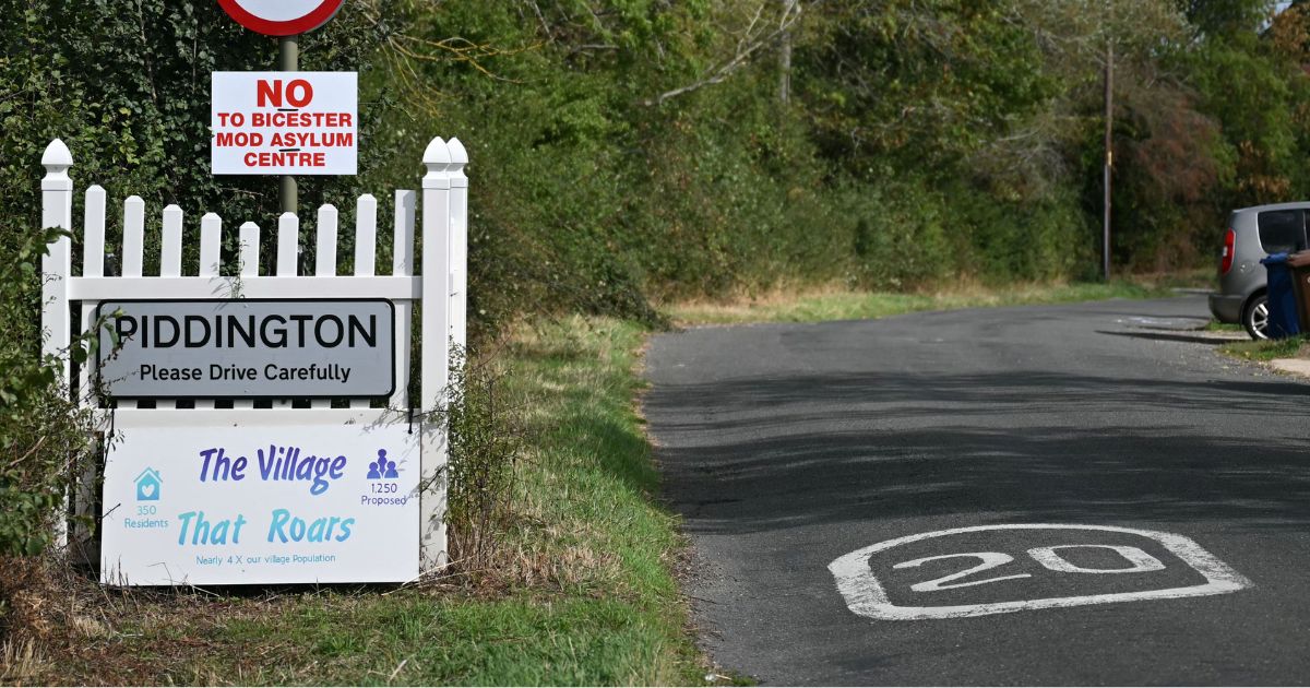 A sign for the village of Piddington, England, is pictured next to another saying 'No to Bicester MOD asylum centre,' in reference to a government plan to house some 1,200 male asylum seekers nearby.