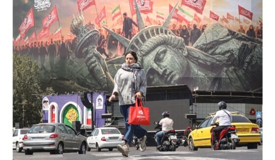 A woman crosses as motorists drive past an anti-US billboard at Enghelab Square in Tehran on Sept. 2.