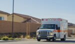 An ambulance driving past suburban houses on a sunny day.