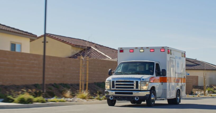 An ambulance driving past suburban houses on a sunny day.