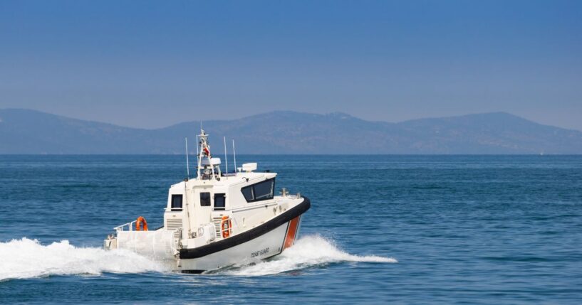 The rear view of a white Coast Guard patrol boat cruising at high speed on blue sea water.