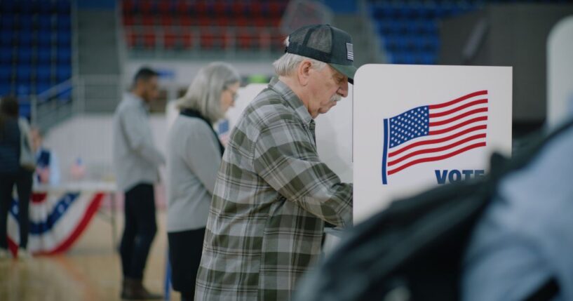A male voter with a bulletin in hand comes to a voting booth.