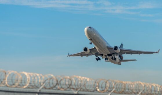 A deportation plane taking off over a barbed wire fence at Miami International Airport.