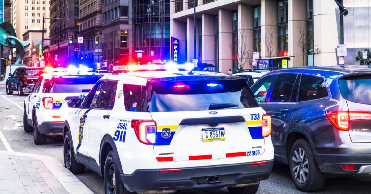 Police vehicles with their lights flashing alongside traffic in downtown Philadelphia.