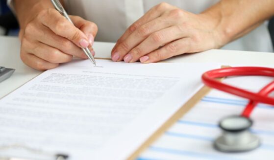 A doctor writes on a note pad beside a stethoscope.
