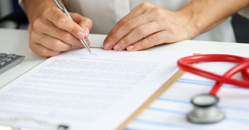 A doctor writes on a note pad beside a stethoscope.