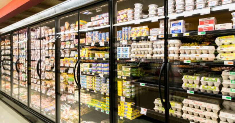 Fridges in a grocery store aisle are illuminated by light.
