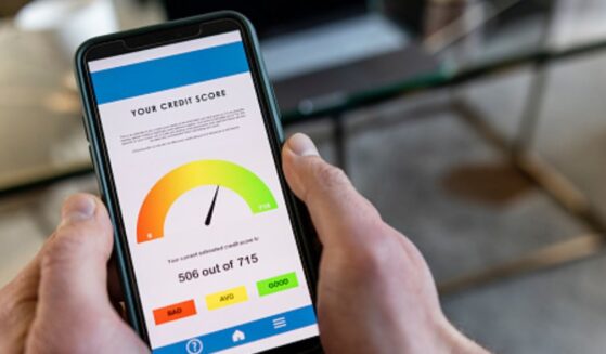 A phone with a credit score displayed on the screen is pictured in a man’s hand.