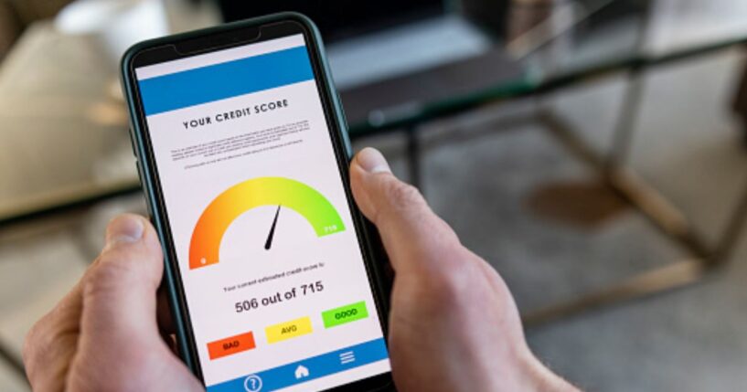 A phone with a credit score displayed on the screen is pictured in a man’s hand.