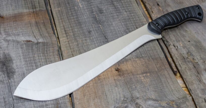A machete is pictured on a wooden table.