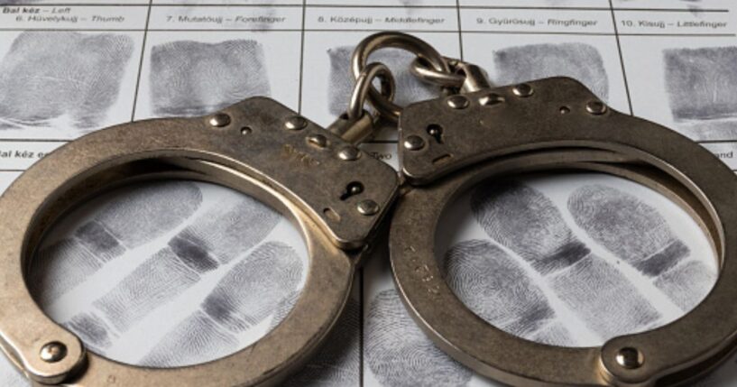 A pair of handcuffs sit on a paper of thumb prints.