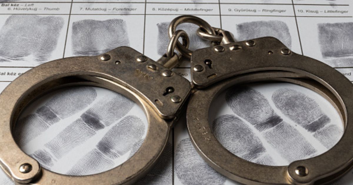 A pair of handcuffs sit on a paper of thumb prints.