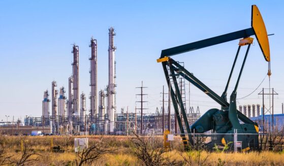 A pumpjack and oil refinery stands in daylight in Seminole, Texas.