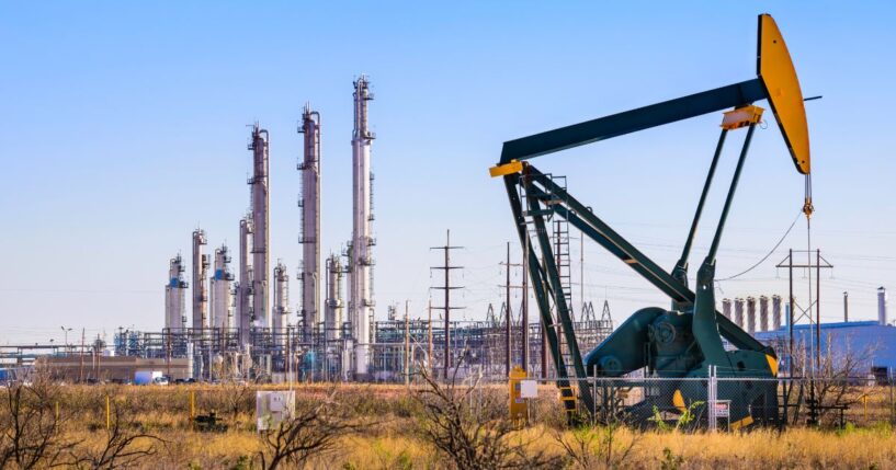 A pumpjack and oil refinery stands in daylight in Seminole, Texas.
