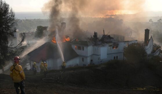 Firefighters spray water on a burning home engulfed by the Norte Fire moving through Southern California on Oct. 16, 2026.