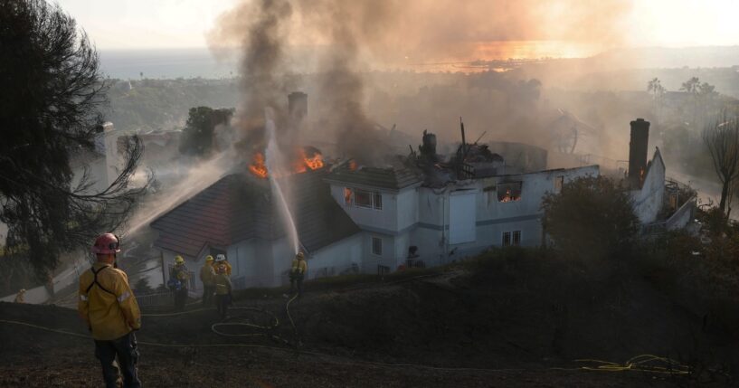 Firefighters spray water on a burning home engulfed by the Norte Fire moving through Southern California on Oct. 16, 2026.